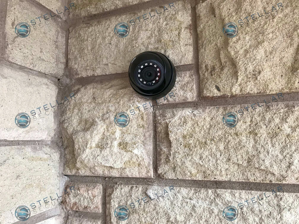 Close-up view of dark turret security camera flush-mounted on textured stone exterior wall in Mississauga