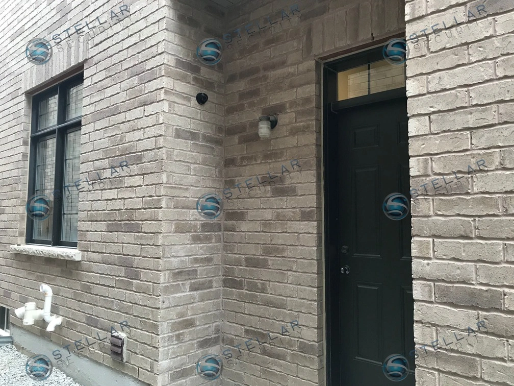 Outdoor security camera mounted on grey brick wall near side door entrance of a Vaughan home
