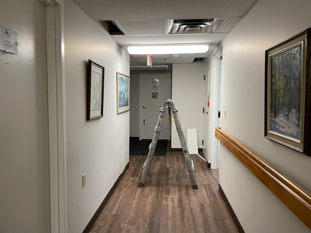 Clean residential corridor with wood handrails, framed art, and stepladder used for mounting ceiling security cameras.