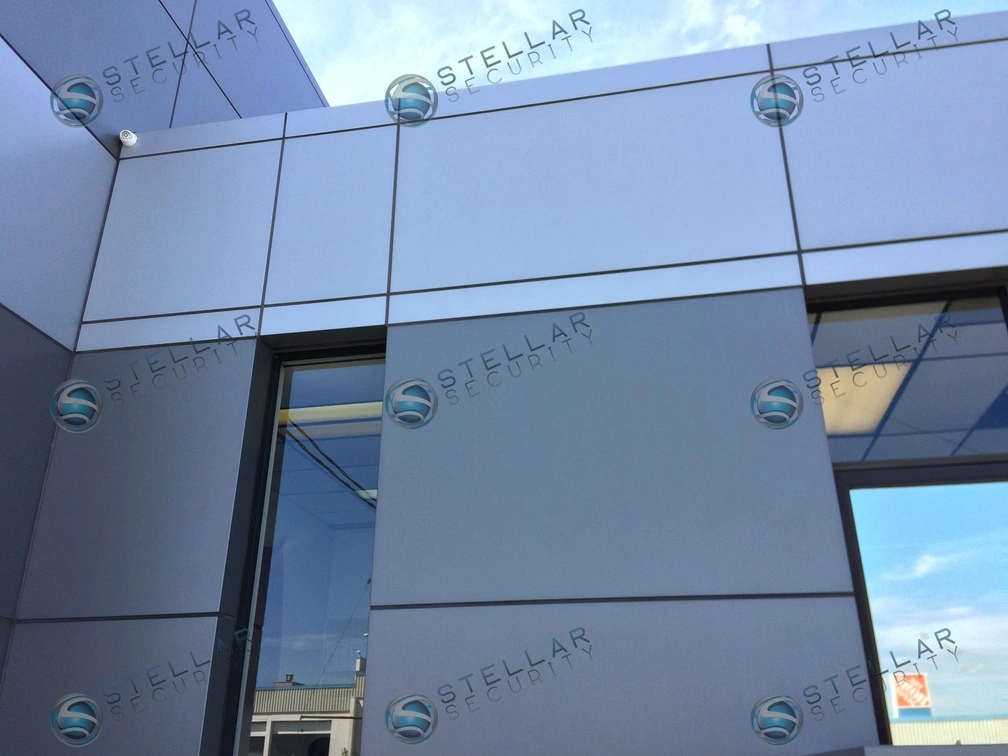 Commercial exterior security camera mounted on aluminum composite wall panel of an auto dealership