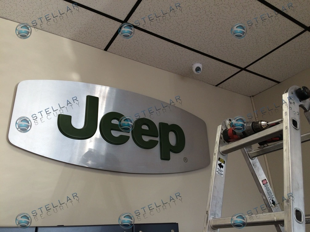 Dome security camera installed on acoustic ceiling tiles above showroom brand signage