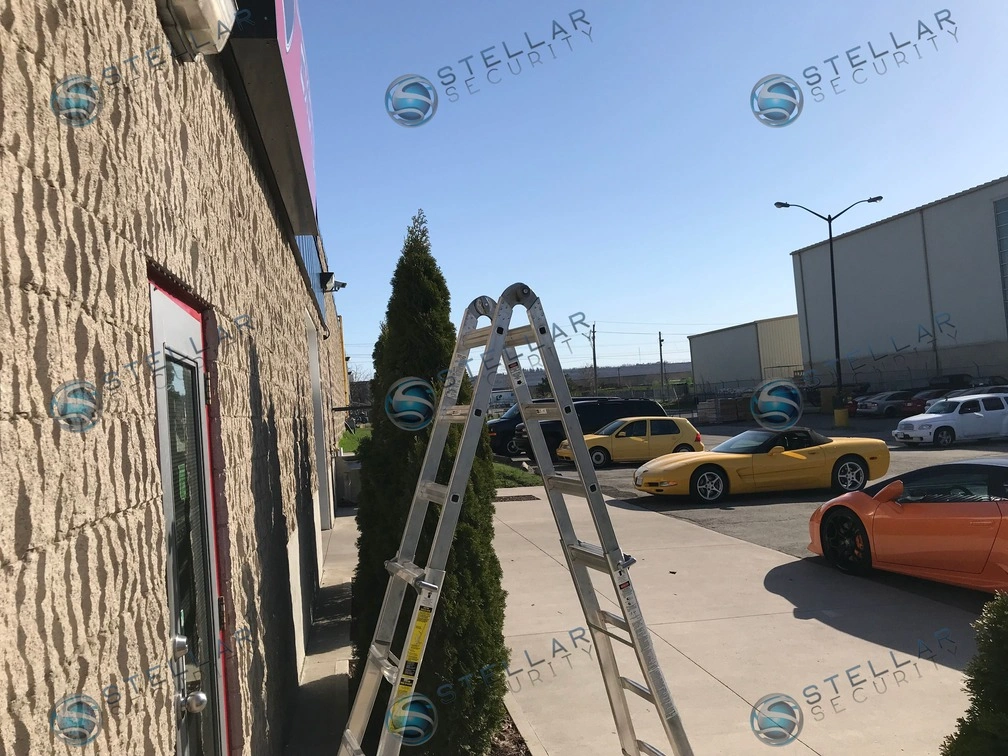 Extension ladder set up along concrete block building wall during commercial security camera installation.
