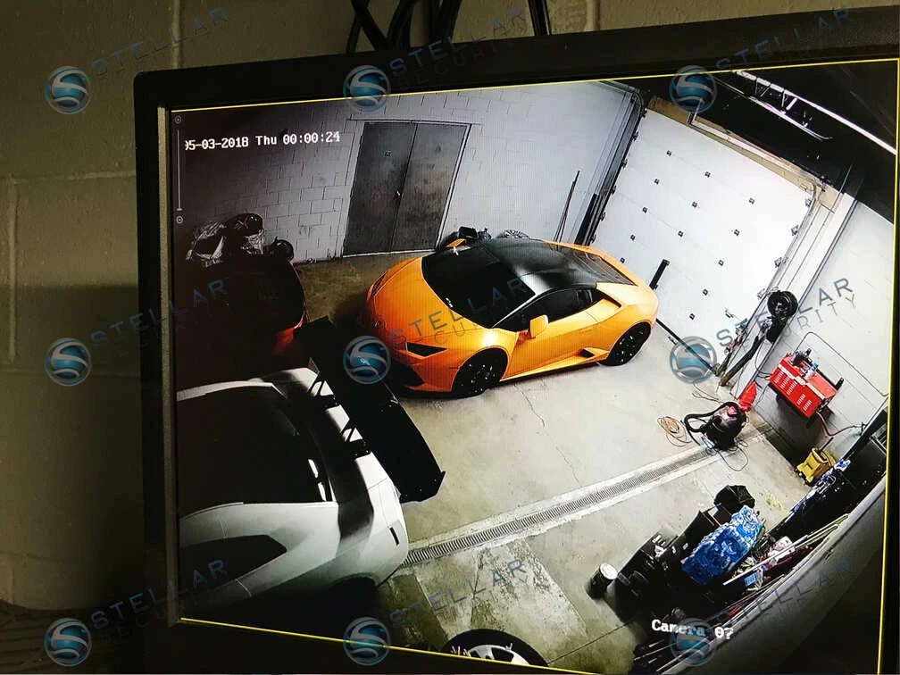 Monitor feed showing high-angle indoor security camera coverage of exotic sports cars parked inside service bay.