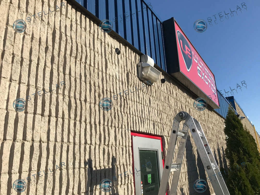 Ladder set up beneath an outdoor security camera installed directly above a commercial shop entrance door.
