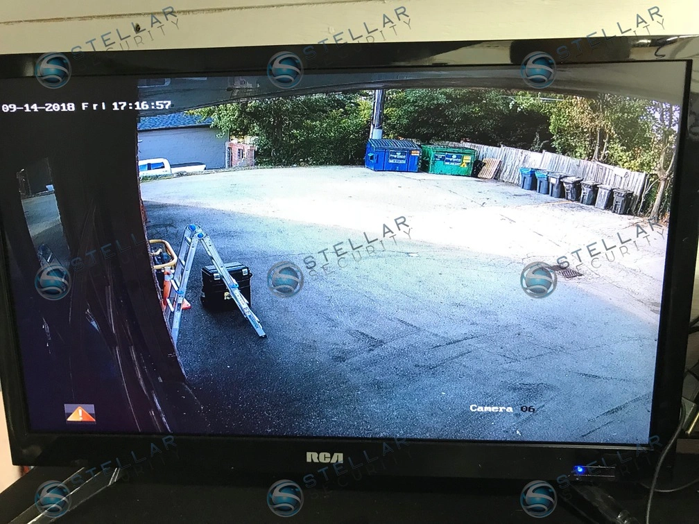 Live surveillance feed on monitor covering shop parking lot, dumpster area, and perimeter driveway
