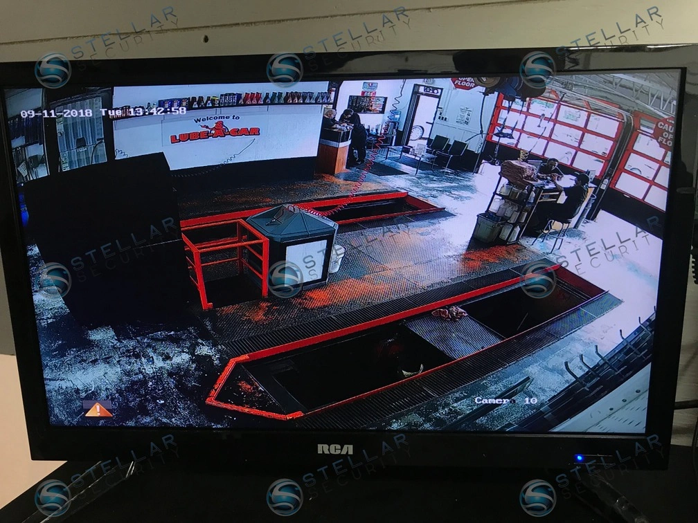 NVR monitor displaying wide-angle live security camera feed of garage service pit and interior work area