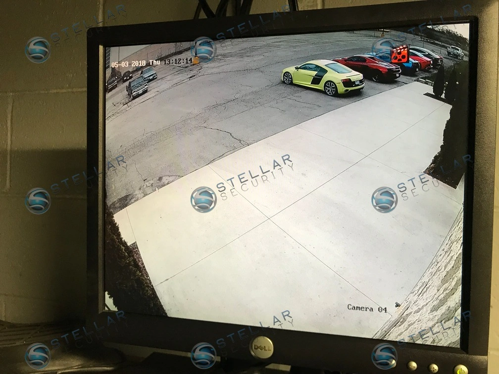 Desktop monitor showing exterior high-definition security camera feed monitoring luxury car parking lot.