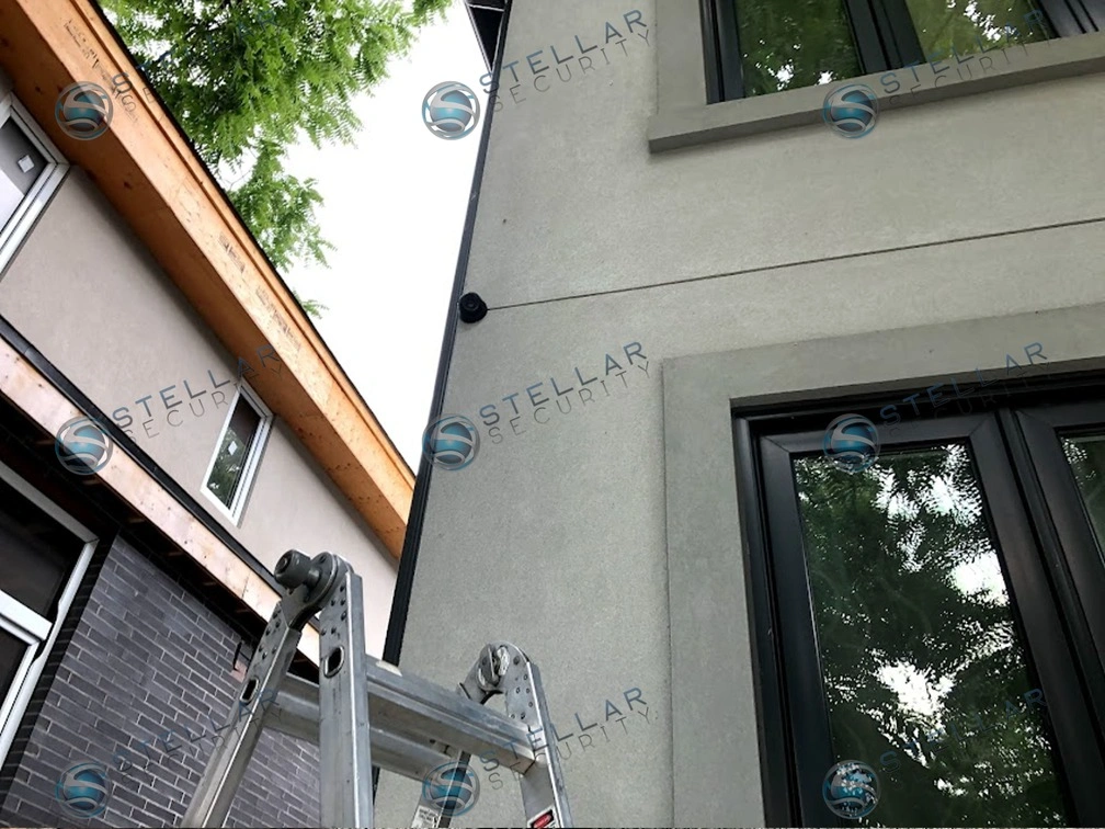 High-reach security camera installed on second-story stucco wall near upper window frame in Etobicoke