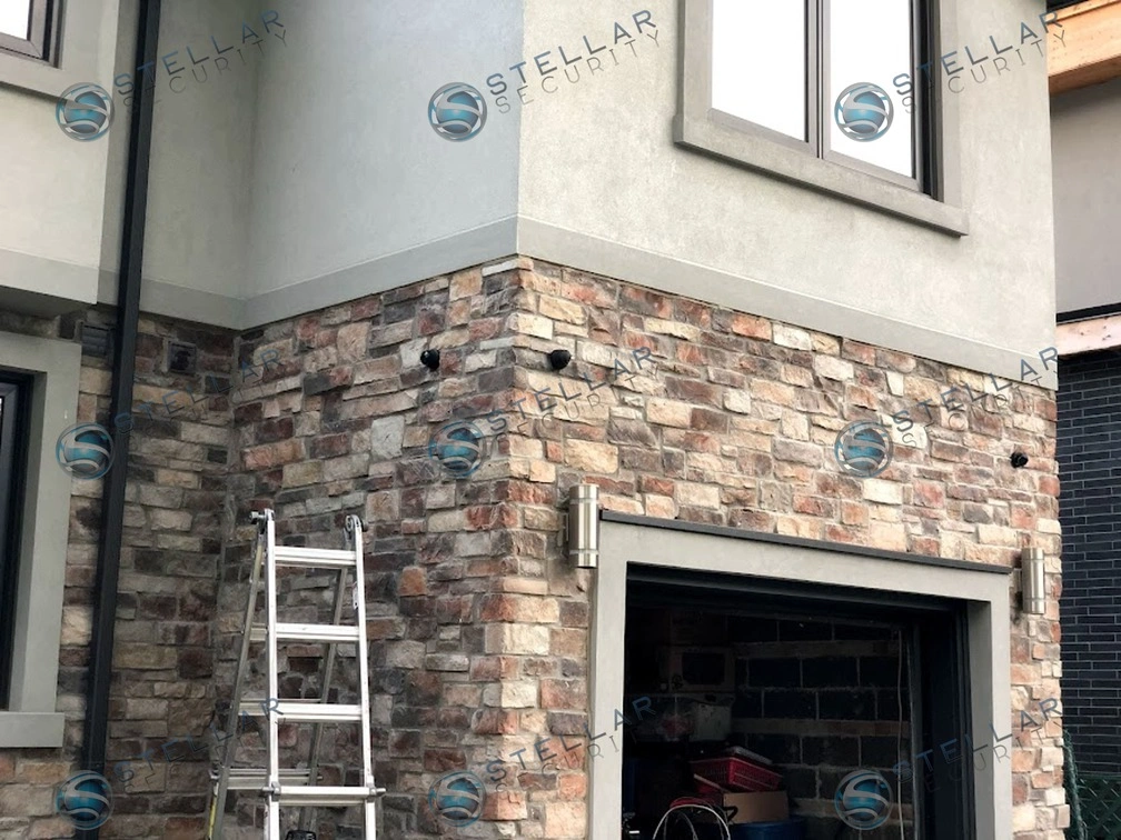 Outdoor security camera mounted on upper stucco wall overlooking garage driveway in Etobicoke