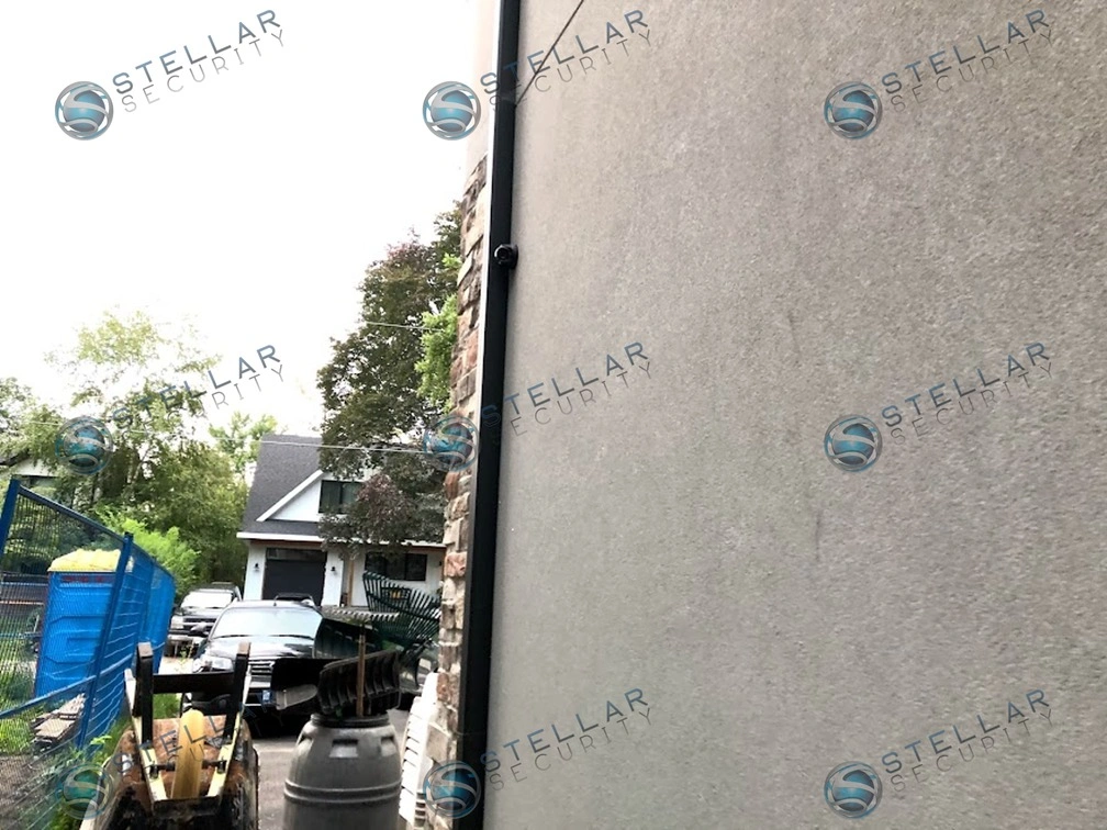 Stucco exterior wall with neatly run dark cable conduit alongside downspout on Etobicoke home