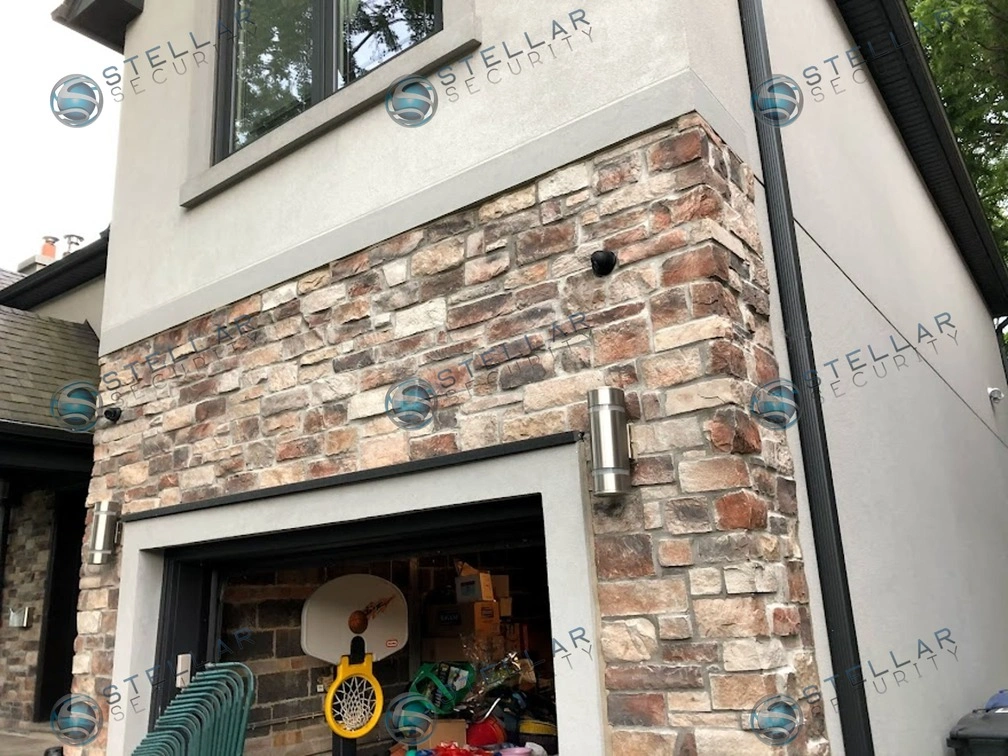 Close-up of black turret camera mounted above garage door on stone masonry facade in Etobicoke