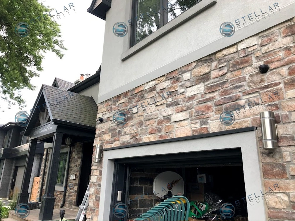 Front view of double garage exterior featuring natural stone trim and mounted security cameras in Etobicoke
