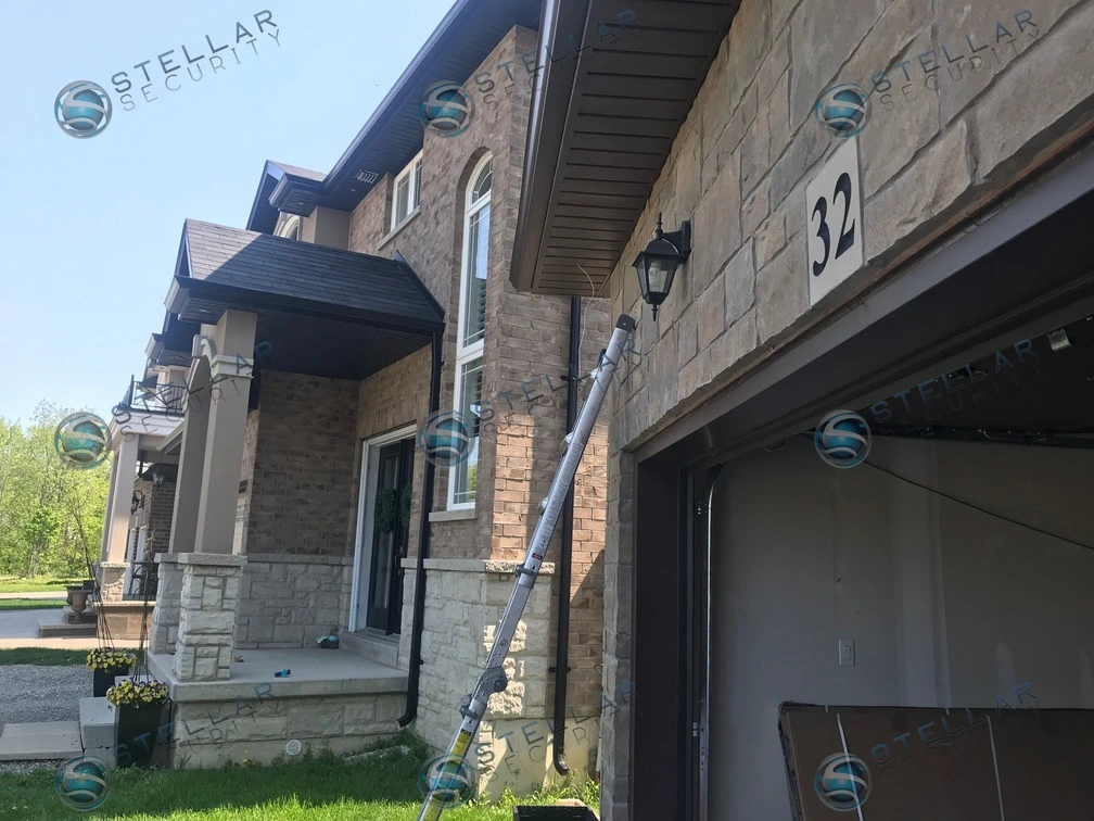 Outdoor security camera mounted on exterior stone wall above house number near garage in Hamilton