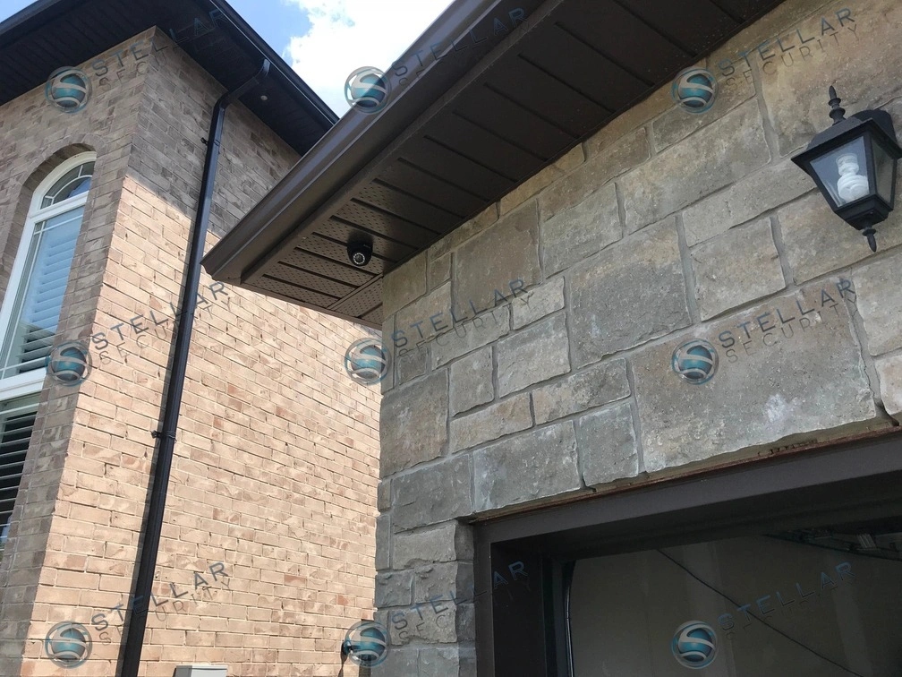 Close-up of black turret security camera mounted under soffit overhang above garage in Hamilton