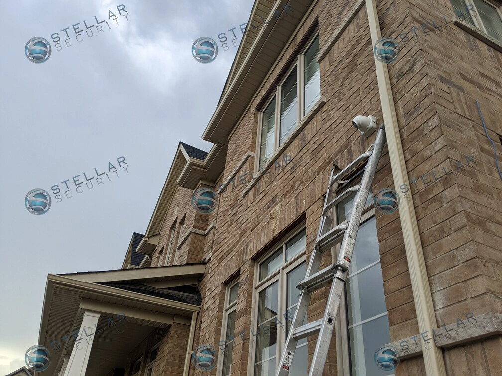 Extension ladder set up for high-reach security camera mounting on brick home exterior in Kitchener