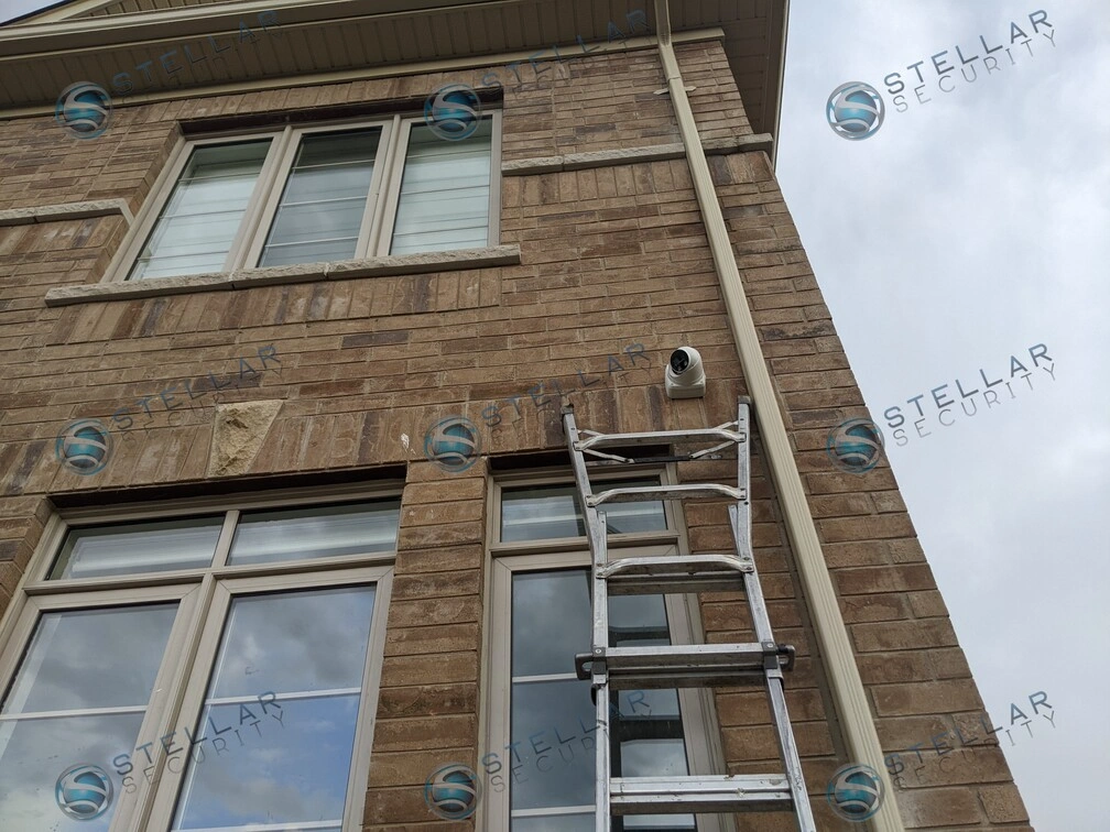 Outdoor security camera installed high on second-story brick wall near window in Kitchener