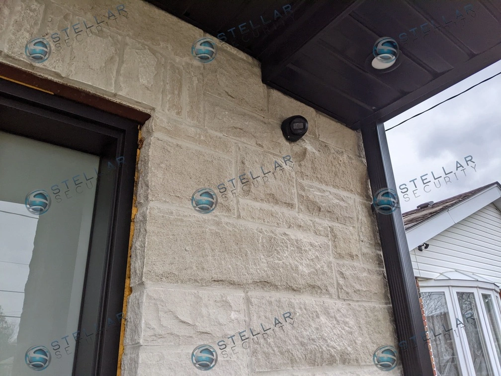 Dark 4K turret security camera mounted on light stone exterior beside front entrance of a London home