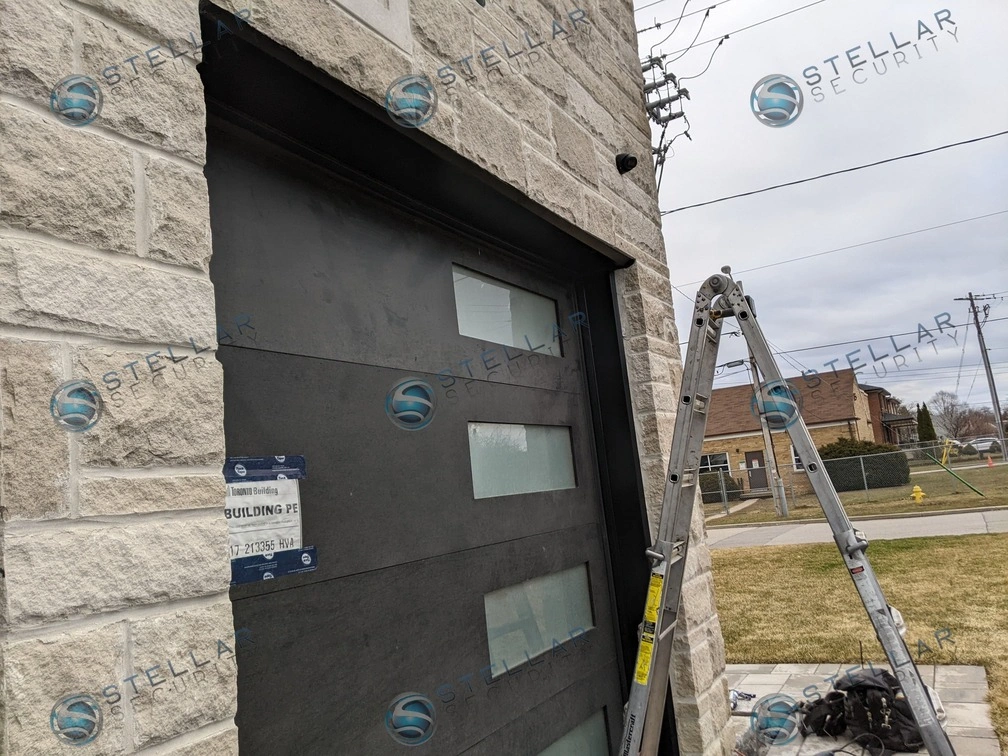 Dark security camera installed on stone facade directly above modern dark garage door in London