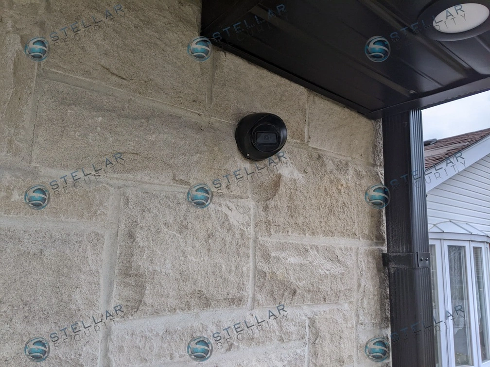 Close-up view of a black outdoor turret security camera mounted flush on a stone exterior wall in London