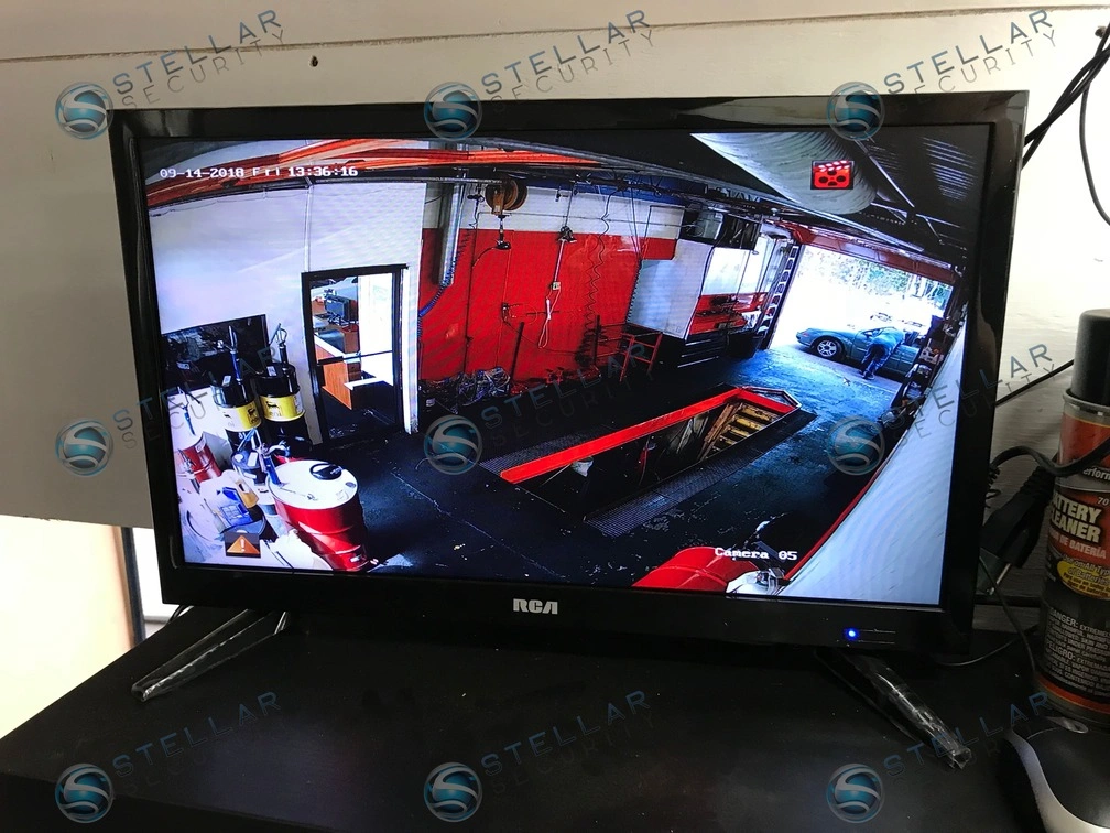 Monitor showing real-time camera view of auto repair bay, tool chests, and vehicle service area