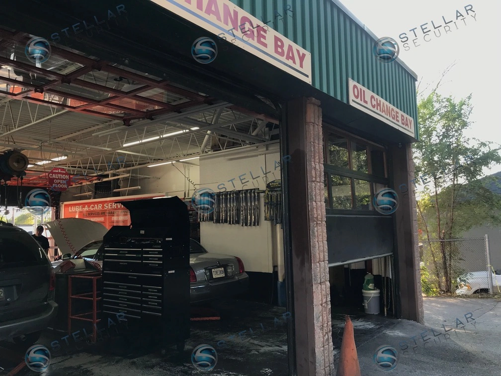 Outdoor security camera mounted above open service bay door overlooking mechanic shop drive-in area