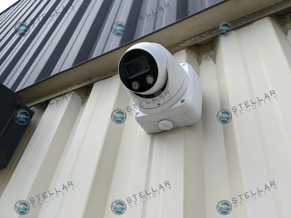 Outdoor turret security camera mounted on a corrugated industrial metal building exterior.