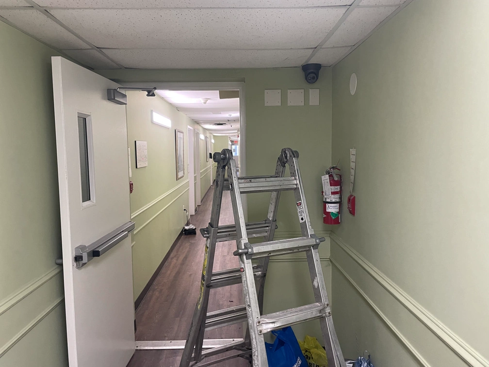Black dome security camera mounted high on green hallway wall above doorway inside senior living facility.
