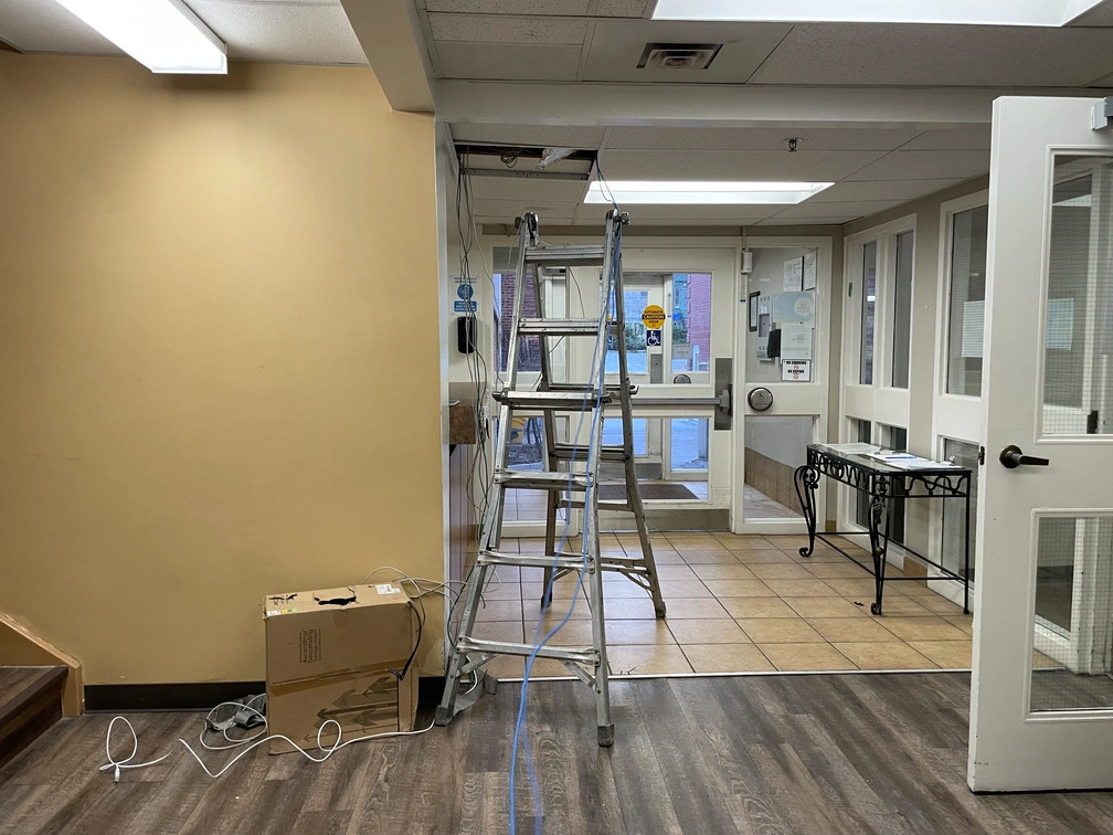 Network cabling pulled through drop ceiling tile above stepladder in retirement home entrance foyer.