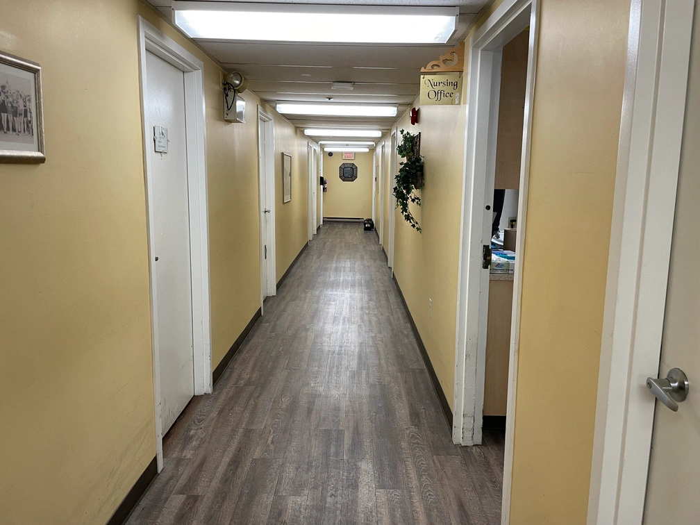 Bright residential hallway featuring wall handrails, wood-look flooring, and ceiling-mounted security cameras outside nursing office.