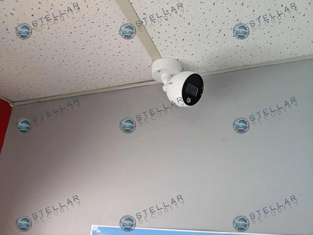 Close-up of a white mini turret security camera mounted neatly to a commercial drop-ceiling tile.
