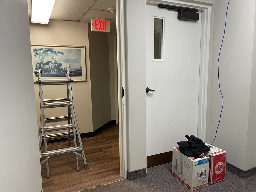 Stepladder and equipment boxes set up near fire door entrance during interior security camera installation.