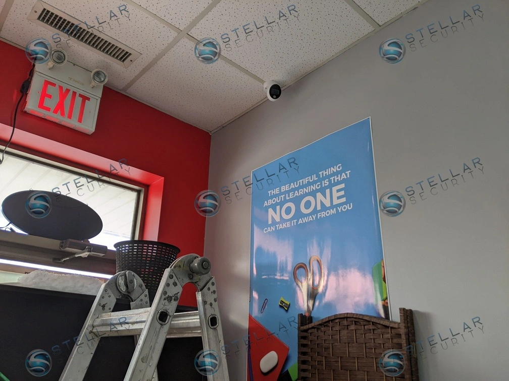 Commercial dome security camera mounted on drop ceiling above a school reception exit door.