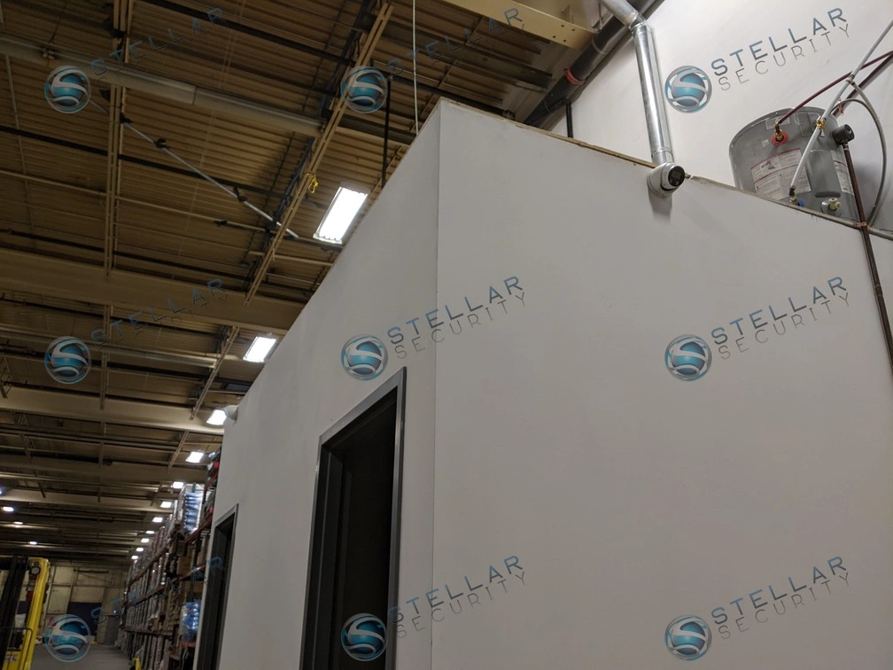 Interior warehouse wall section with high-mounted security camera overlooking storage racks.