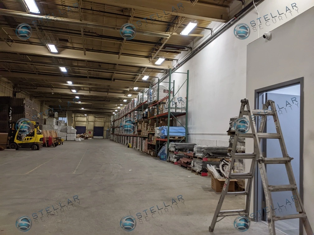 High-ceiling warehouse storage aisle monitored by a wide-angle indoor commercial security camera.