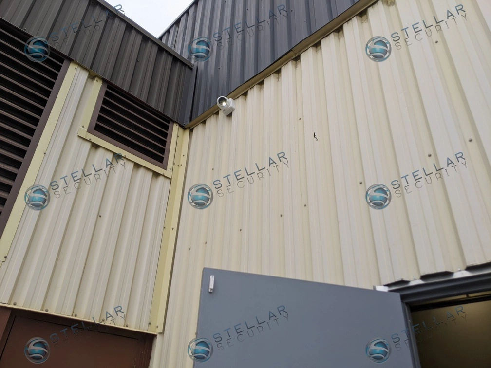 High-angle view of a commercial security camera mounted on corrugated industrial siding.